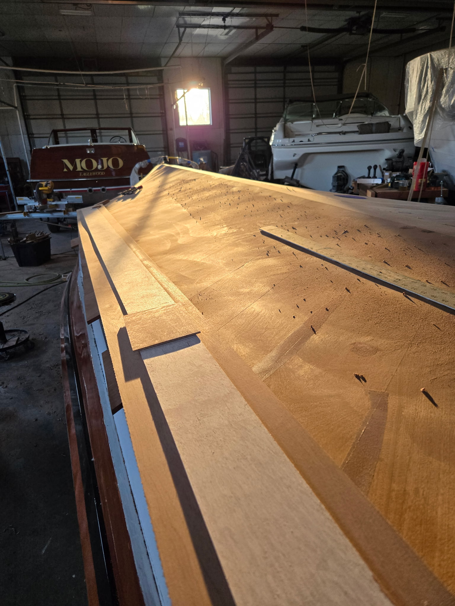 Freshly sanded bare mahogany boat deck in golden shop light, ready for varnish.