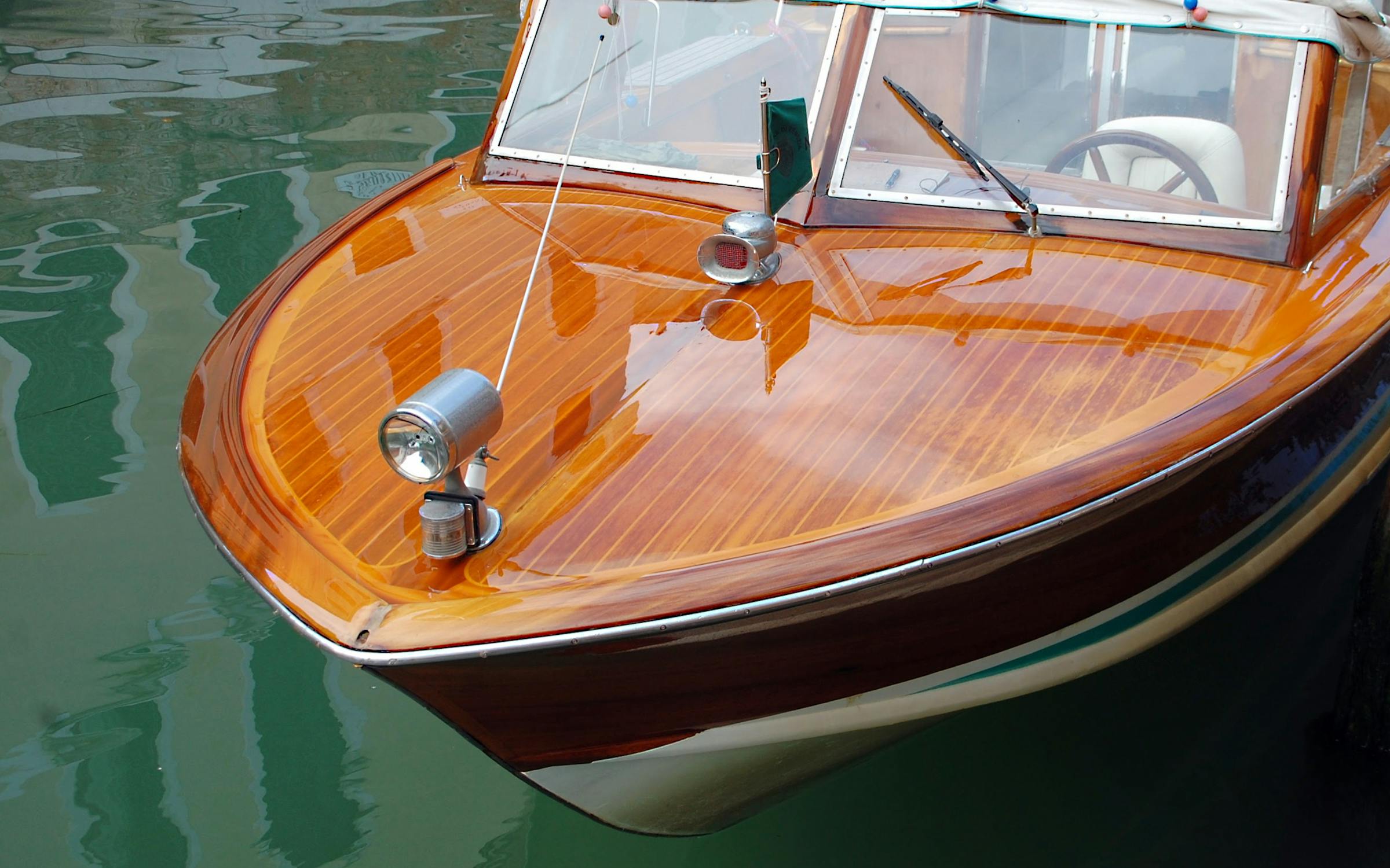Detail of a classic mahogany boat reflecting on calm water.